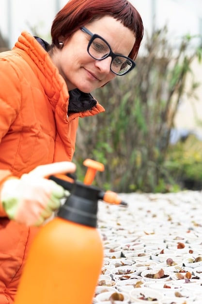 A homeowner is shown spraying a natural flea and tick repellent around the perimeter of their yard. The yard is well-maintained with a green lawn and trimmed bushes. The homeowner is wearing protective gloves and eye protection, ensuring safe application of the product.