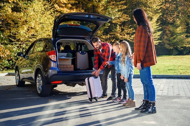 A family putting luggage and a pet carrier into a car, preparing to evacuate their home.