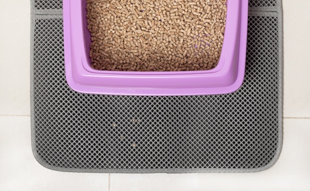 A cat using a litter box with a patterned litter mat placed underneath. The mat is effectively catching loose litter, preventing it from spreading onto the floor.